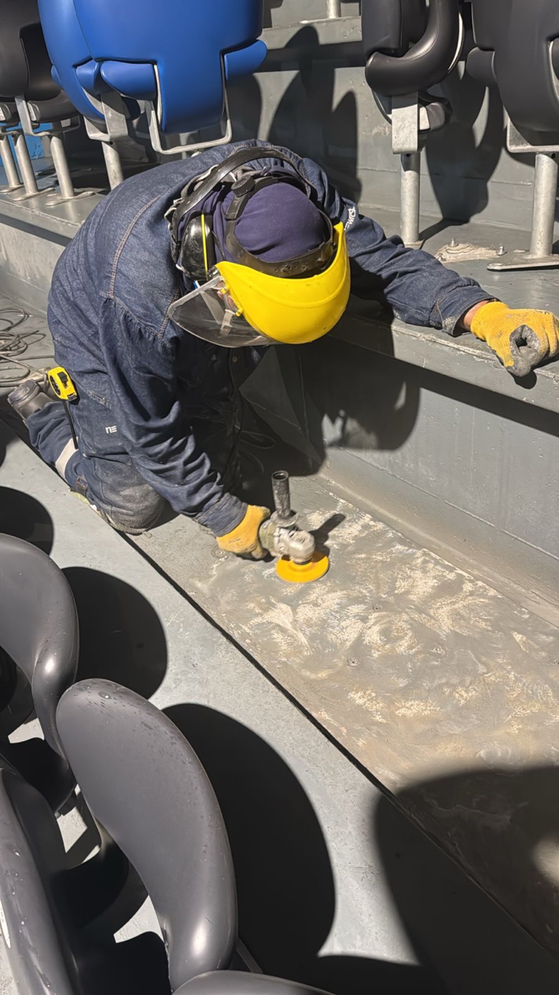 Técnico con uniforme, protección facial y guantes preparando una superficie industrial
